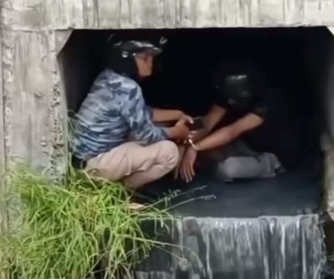 Salah seorang terduga pencuri diborgol polisi di saluran air di Kedung Cowek Surabaya untuk menghindari amukan massa, Senin (18/3/2024). (Catur/kabarterdepan.com) 