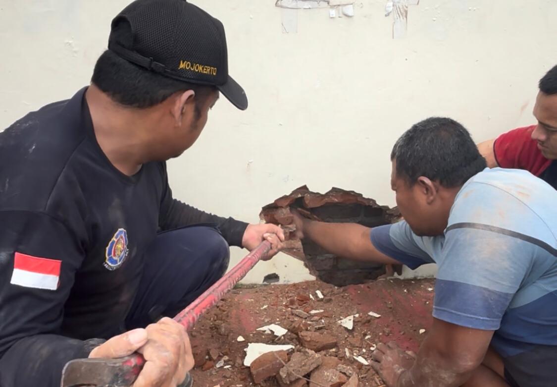 Proses evakuasi handphone warga yang dilakukan Petugas Damkar Kota Mojokerto dengan menjebol dindinglapangan GOR Ahmad Yani Kelurahan Wates, Kecamatan Magersari, Kota Mojokerto, Rabu (8/1/2025) pagi (Andy / Kabarterdepan.com) 