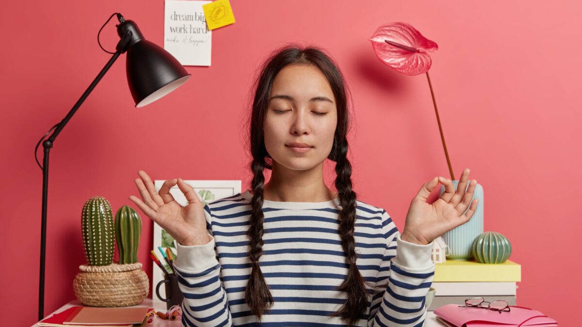 relaxed asian woman meditates workplace sits zen pose against desktop with flowers desk lamp notepads wears striped casual jumper tries relax after work isolated pink background 1 relaxed asian woman meditates workplace sits zen pose against desktop with flowers desk lamp notepads wears striped casual jumper tries relax after work isolated pink background