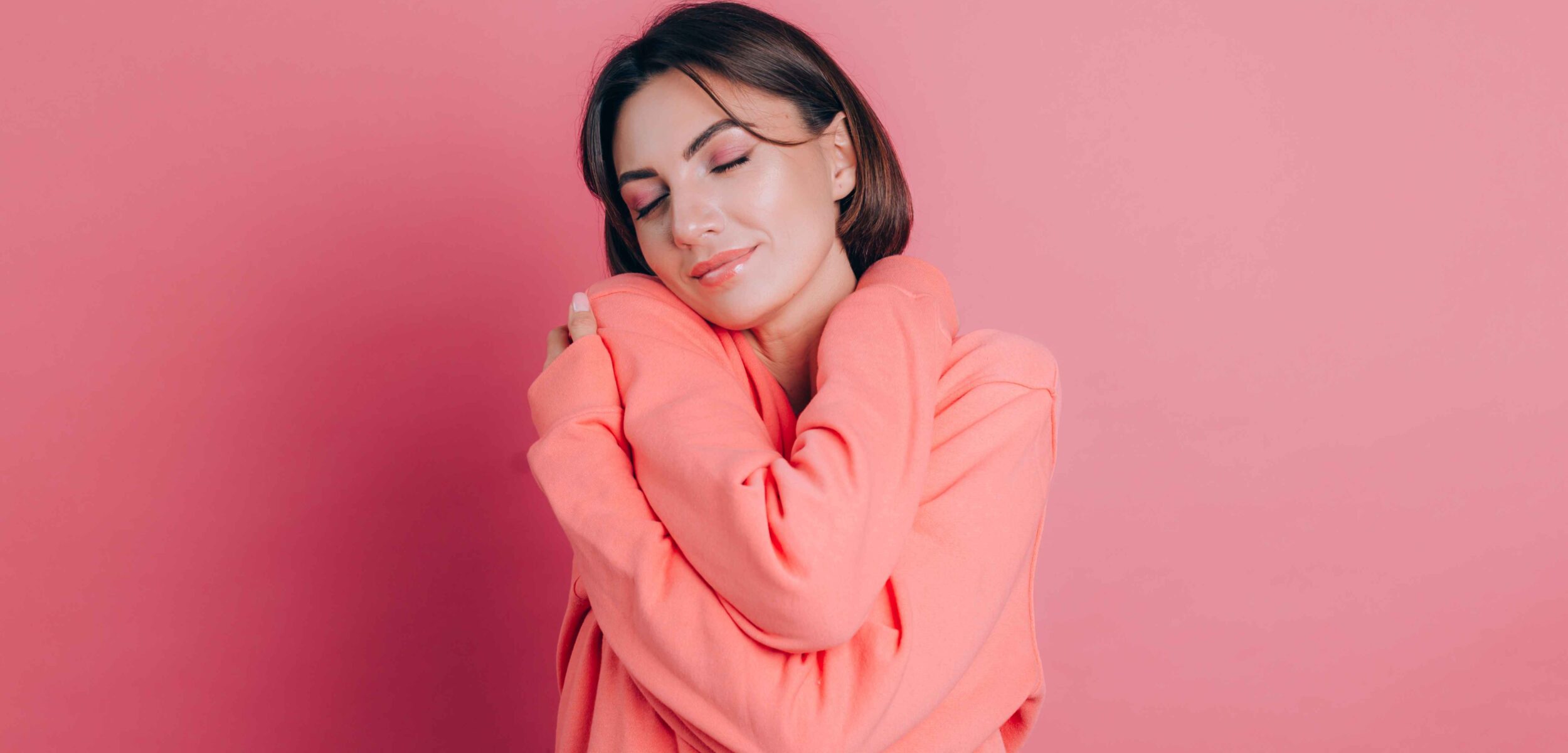 smiling young woman 20s casual clothes isolated pink background studio portrait love concept keeping eyes closed holding hands crossed hugging herself 11zon