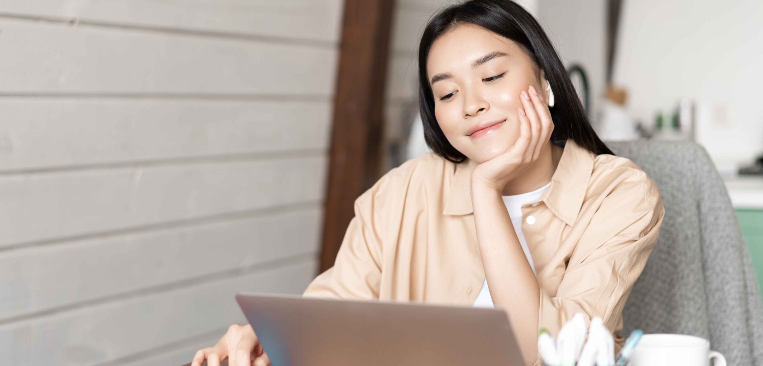 smiling asian girl student woman sitting with laptop home kitchen browing smartphone social media 11zon